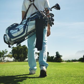 Man walking on golf course with clubs over his shoulder on a sunny day