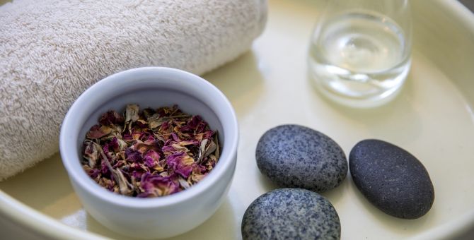 A tray in spa filled with a towel, potpourri, hot stones and a glass of water.