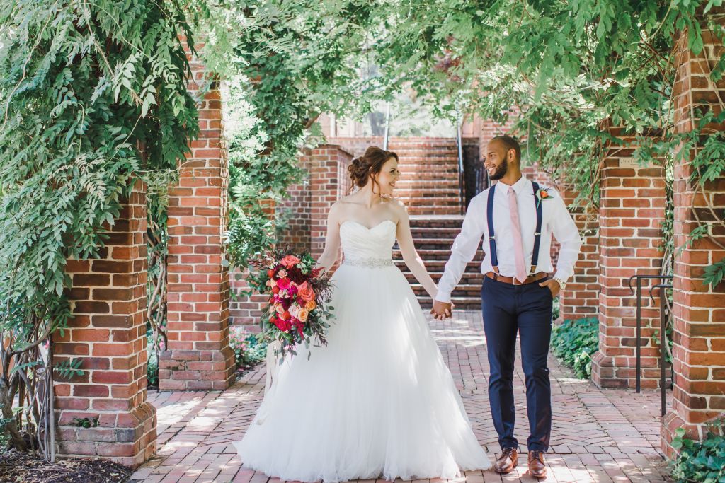 bride and groom holding hands in brick path under cover of wisteria