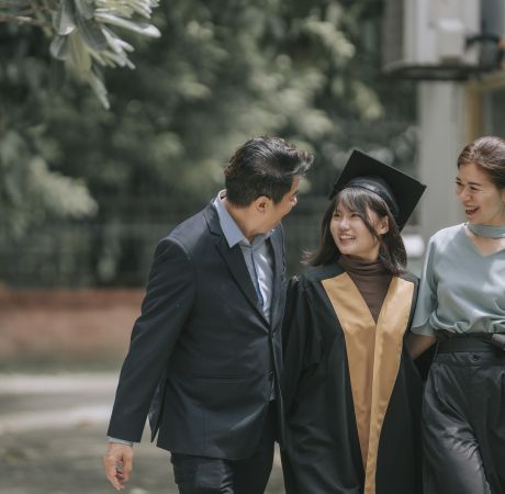 Proud Chinese parents walking together with daughter with graduation gowns in college